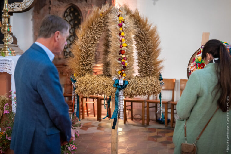 Besucher betrachten eine kunstvoll gebundene Erntekrone in einer Kirche