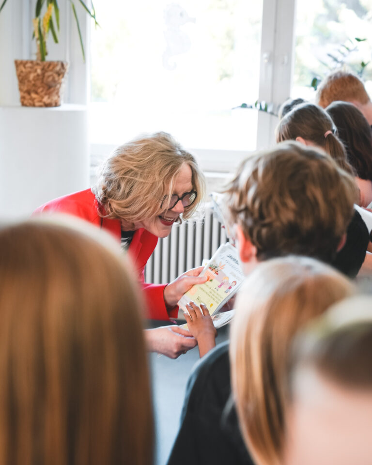 Staatsministerin Regina Kraushaar übergibt Kindern den Schuljahresplaner.