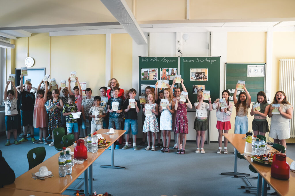 Grundschulkinder präsentieren gemeinsam mit Staatsministerin Regina Kraushaar den Schuljahresplaner 2026/2027.