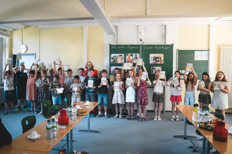 Grundschulkinder präsentieren gemeinsam mit Staatsministerin Regina Kraushaar den Schuljahresplaner 2026/2027.
